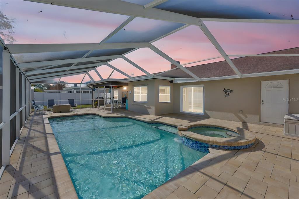 A screened-in patio features a swimming pool, a raised spa, and light-colored stone pavers — 9275 133RD STREET, SEMINOLE, FL