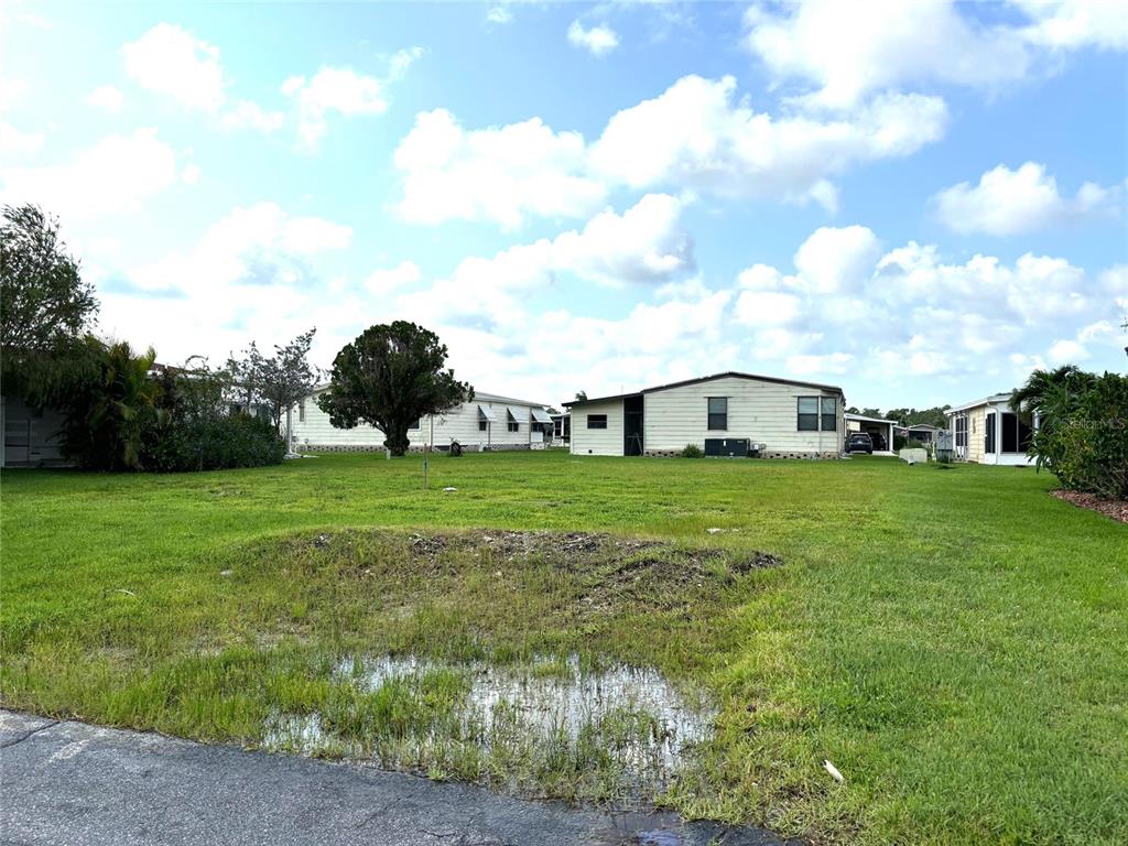 A grassy, vacant lot with a small puddle in the foreground and neighboring mobile homes — 404 TARDE LOGO CIRCLE, NORTH PORT, FL