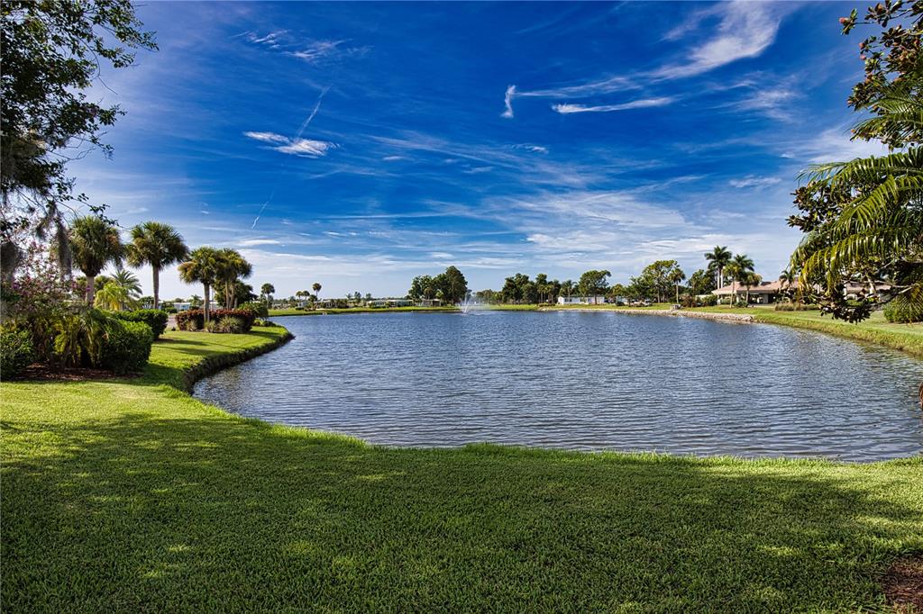 A grassy lawn overlooks a pond with a fountain and palm trees under a blue sky — 404 TARDE LOGO CIRCLE, NORTH PORT, FL