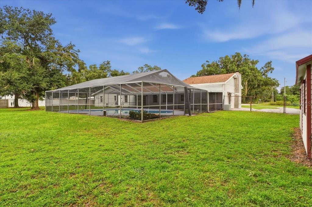 A backyard view of a house with a screened-in swimming pool and a large lawn — 2925 MCGEE ROAD, PLANT CITY, FL