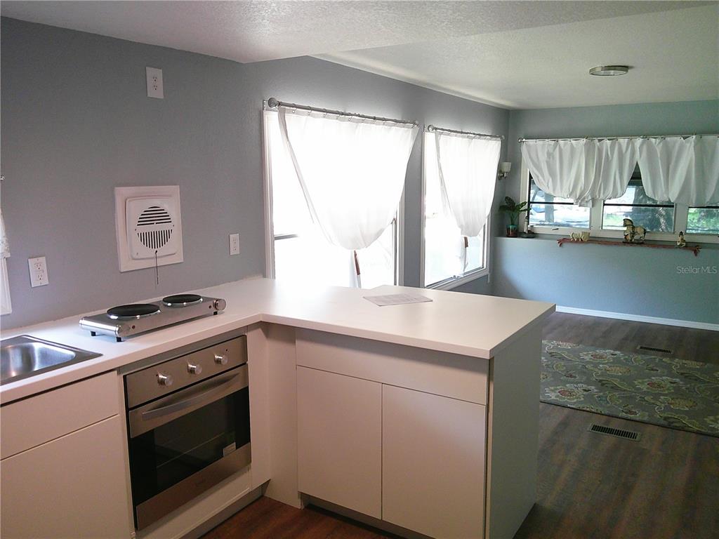 A kitchen with white cabinets and a peninsula counter overlooks a room with wood flooring — 6250 CONNECTICUT STREET, ZEPHYRHILLS, FL
