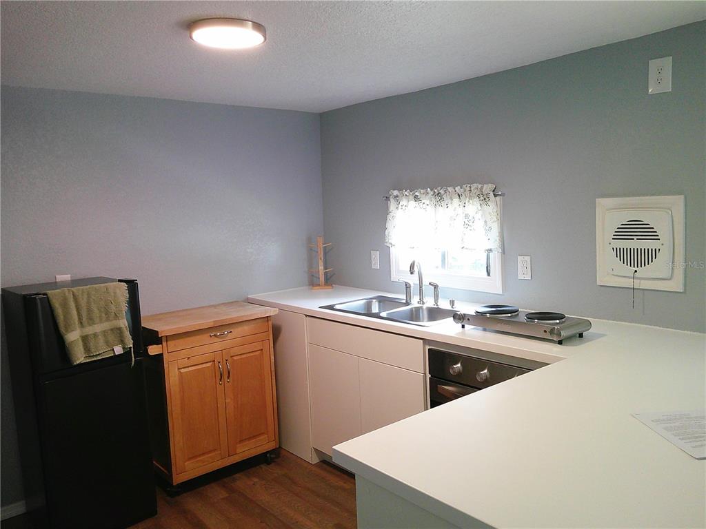 A kitchen with white cabinets, a built-in oven, and a cooktop overlooks a living area — 6250 CONNECTICUT STREET, ZEPHYRHILLS, FL