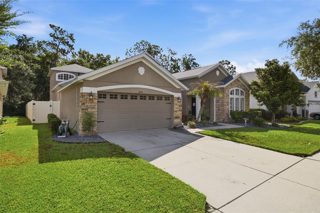 A single-story suburban house with a two-car garage, stone accents, and a concrete driveway — 6846 PINE SPRINGS, WESLEY CHAPEL, FL
