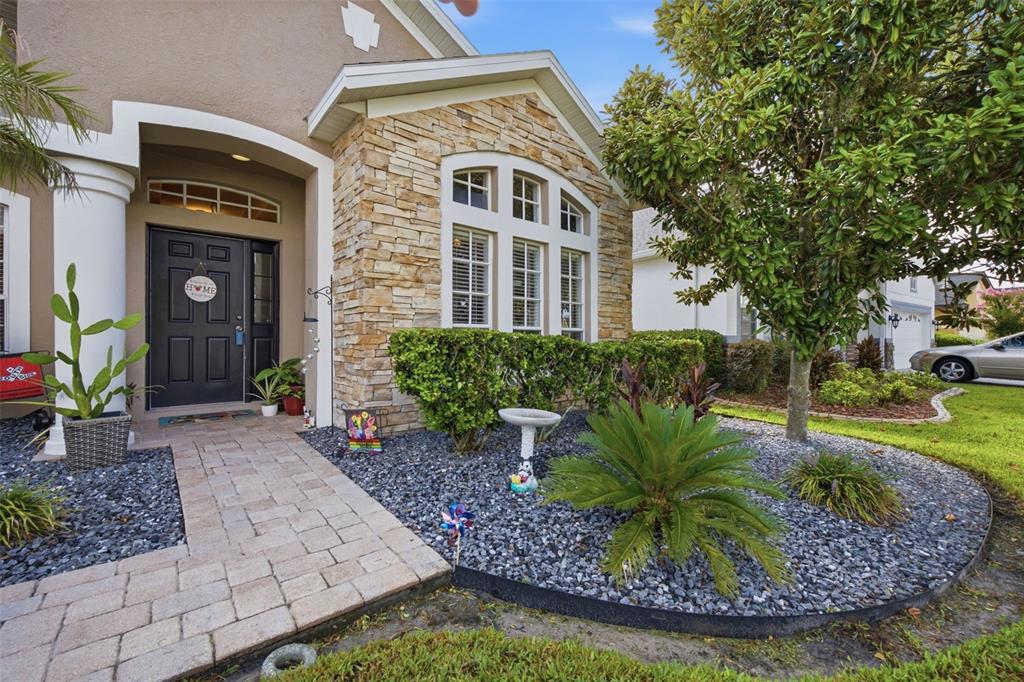 The exterior of a house features a stone facade, a paved walkway, and landscaping — 6846 PINE SPRINGS, WESLEY CHAPEL, FL