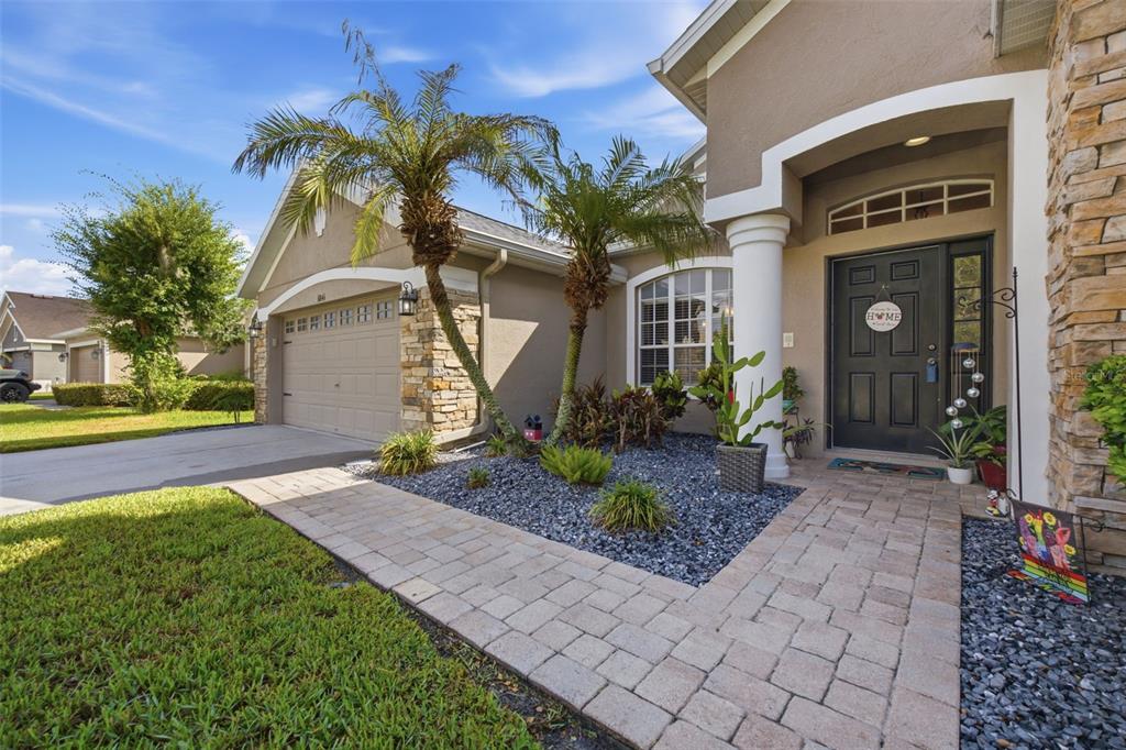 A paved walkway leads to the front entrance of a house with a stone-accented garage — 6846 PINE SPRINGS, WESLEY CHAPEL, FL