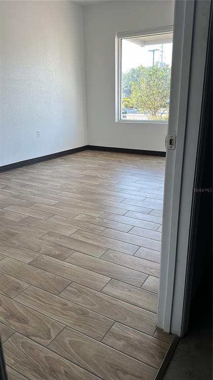 An empty room with light wood-look tile flooring and a window overlooking a parking lot — 1550 TILESTON ROAD UNIT 108, ST CLOUD, FL