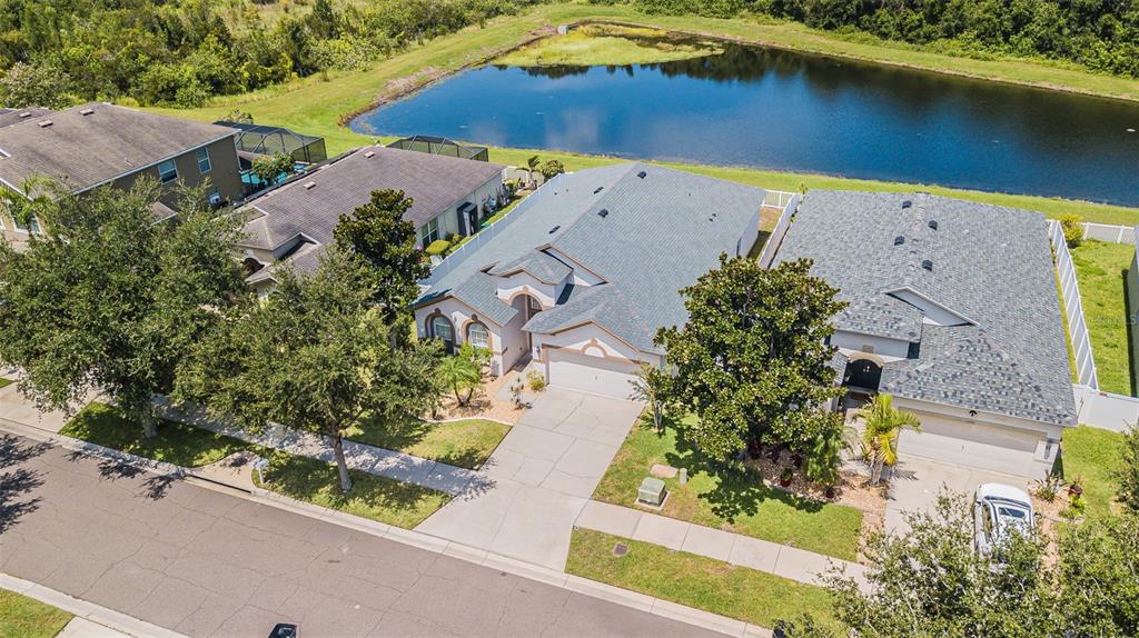 An aerial view shows a suburban street with houses, driveways, and a large retention pond — 11345 FLORA SPRINGS DRIVE, RIVERVIEW, FL