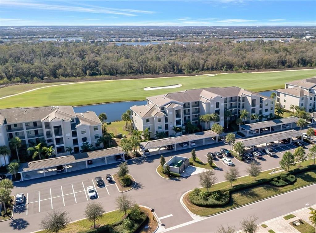 An aerial view shows multi-story apartment buildings with covered parking lots next to a golf course — 17902 GAWTHROP DRIVE UNIT 401, BRADENTON, FL