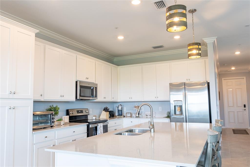 A modern kitchen features white cabinetry, stainless steel appliances, and a large quartz-topped island — 17902 GAWTHROP DRIVE UNIT 401, BRADENTON, FL