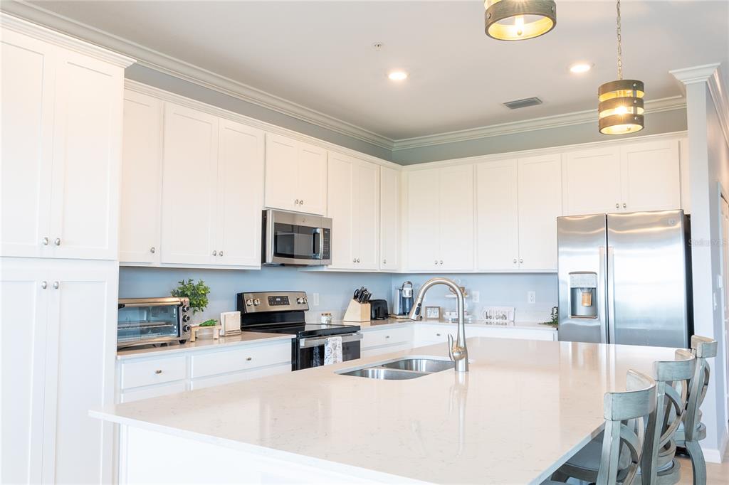 A modern kitchen features white cabinetry, stainless steel appliances, and a large quartz-topped island — 17902 GAWTHROP DRIVE UNIT 401, BRADENTON, FL