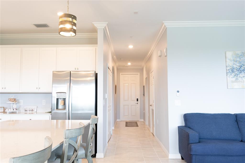 A kitchen with white cabinets and a stainless refrigerator opens to a hallway and living area — 17902 GAWTHROP DRIVE UNIT 401, BRADENTON, FL