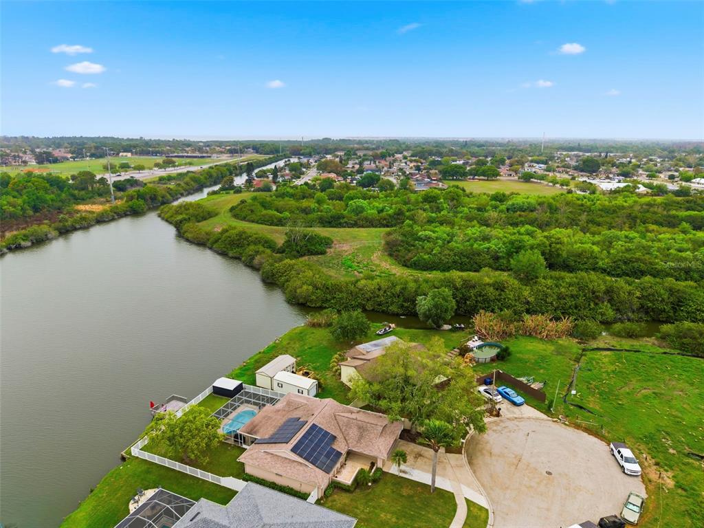 An aerial view shows a waterfront house with a pool, solar panels, and a driveway — 3022 JACKSON DRIVE, HOLIDAY, FL