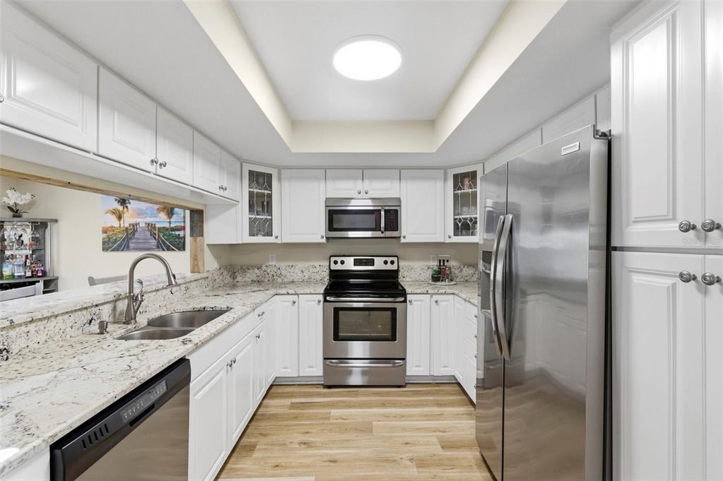 A kitchen with white cabinets, granite countertops, stainless steel appliances, and wood-look flooring — 3022 JACKSON DRIVE, HOLIDAY, FL