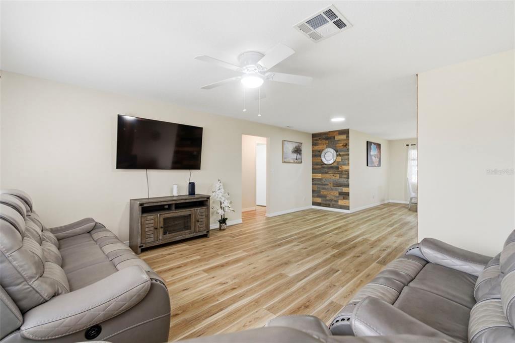 A living room features light wood-look flooring, a wall-mounted television, and a wood-plank accent wall — 3022 JACKSON DRIVE, HOLIDAY, FL