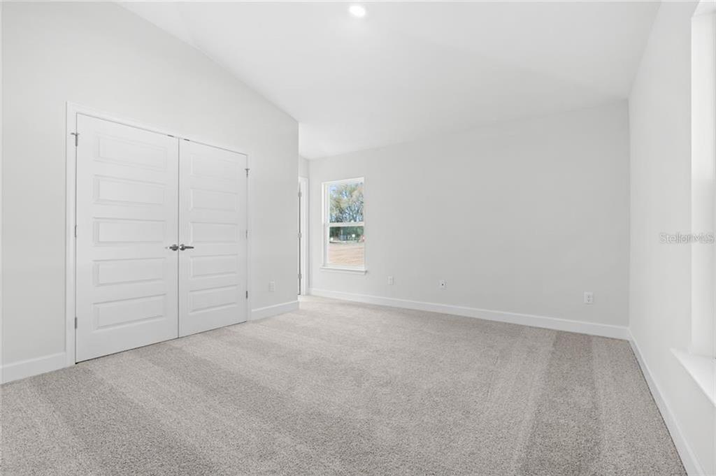 A bedroom with light gray walls, gray carpet, and white double closet doors — 87 RAMBLEWOOD DRIVE, PALM COAST, FL