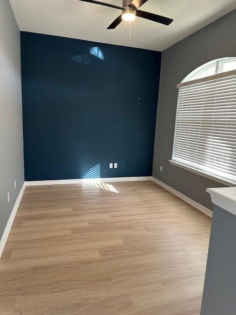 An empty room features light wood-look flooring, a dark blue accent wall, and a large window — 16758 ABBEY HILL COURT, CLERMONT, FL