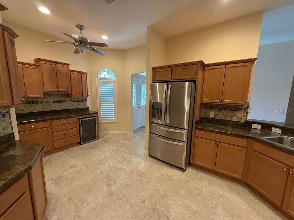 A kitchen with wood cabinets, dark countertops, stainless steel appliances, and light tile flooring — 3578 OBRIEN PLACE, THE VILLAGES, FL