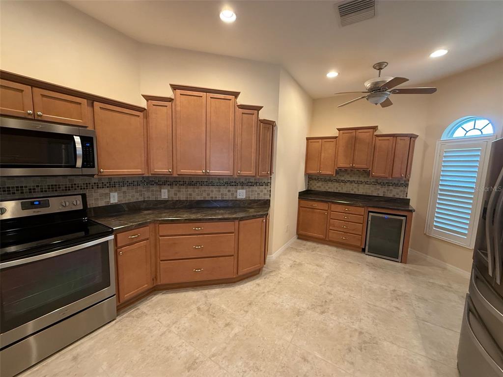 A kitchen features light wood cabinets, dark countertops, stainless steel appliances, and tile flooring — 3578 OBRIEN PLACE, THE VILLAGES, FL