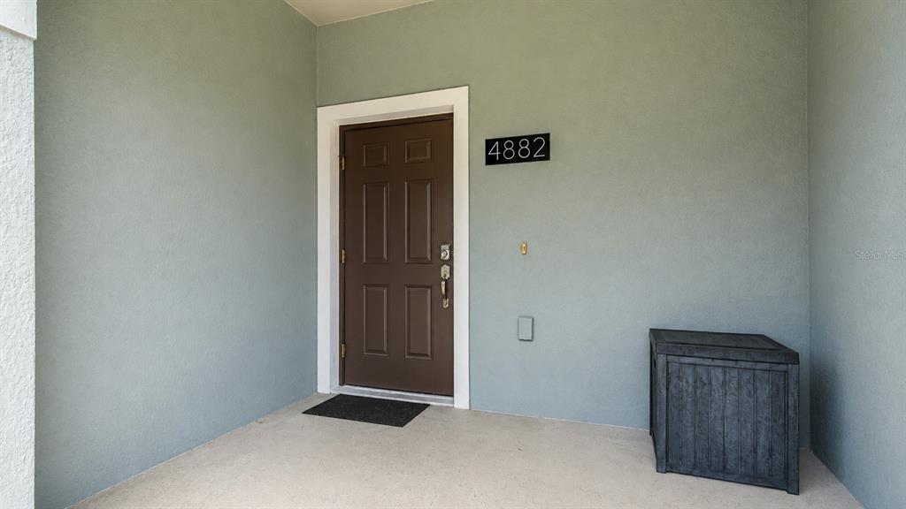 A front porch features a brown door, a house number, and a dark storage bin — 4882 CLOCK TOWER DRIVE, KISSIMMEE, FL