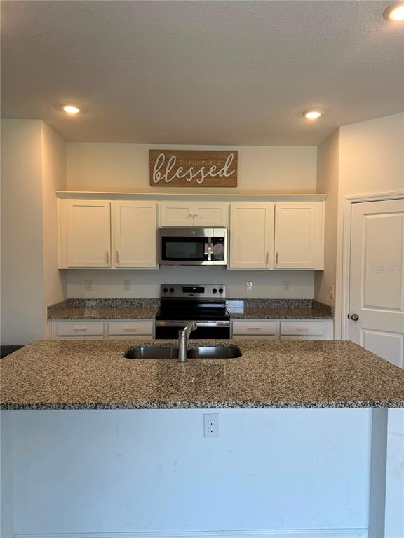 A kitchen features white cabinets, granite countertops, a stainless steel microwave, and a center island — 1457 DALKEITH COVE, SANFORD, FL
