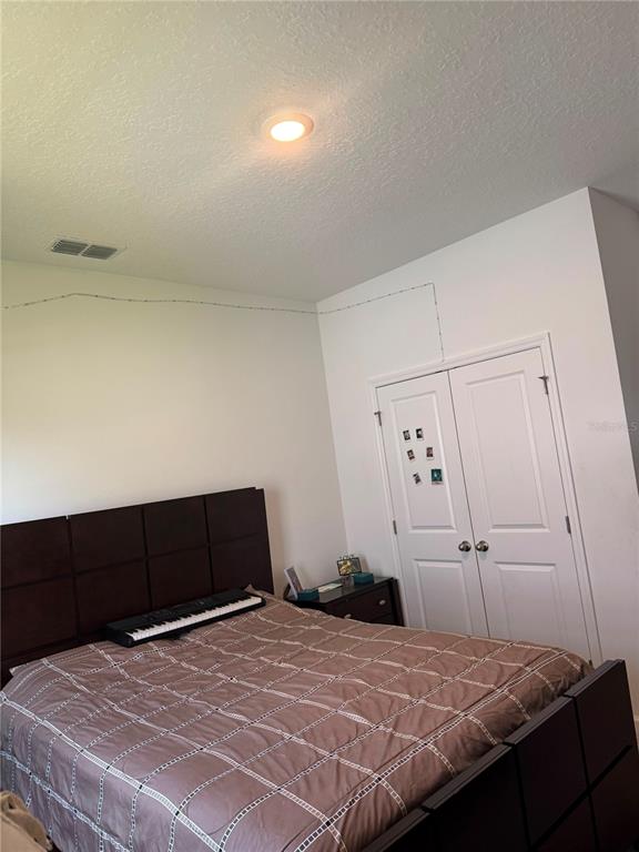A bedroom features a dark wood headboard, a bed with a patterned comforter, and white doors — 1457 DALKEITH COVE, SANFORD, FL