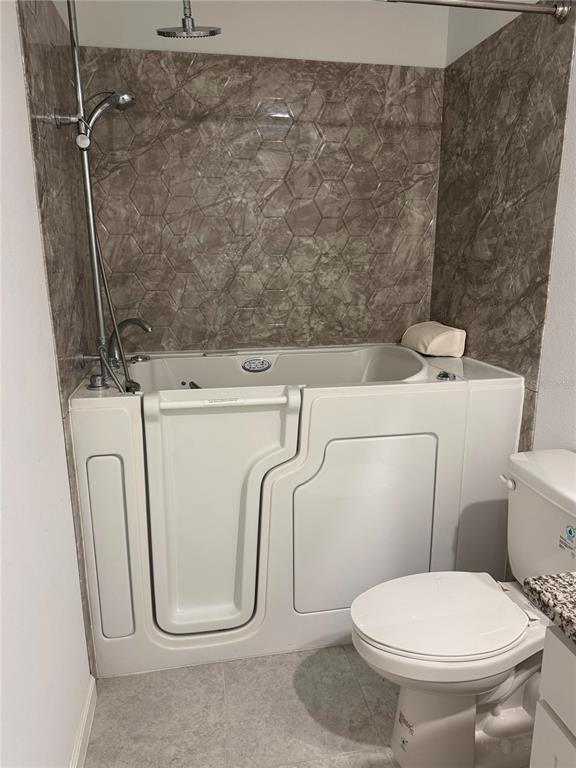 A bathroom features a white walk-in bathtub with a showerhead against a marble-patterned tiled wall — 1457 DALKEITH COVE, SANFORD, FL