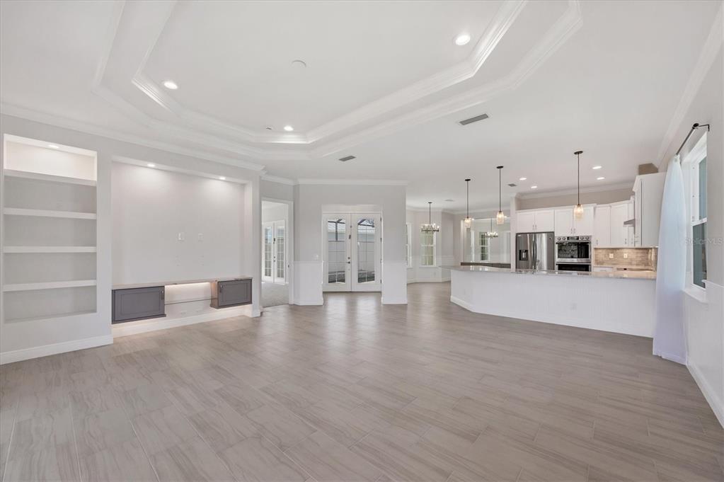 A spacious living room with light wood-look tile floors, a tray ceiling, and an open kitchen — 8936 CONCH AVENUE, PLACIDA, FL