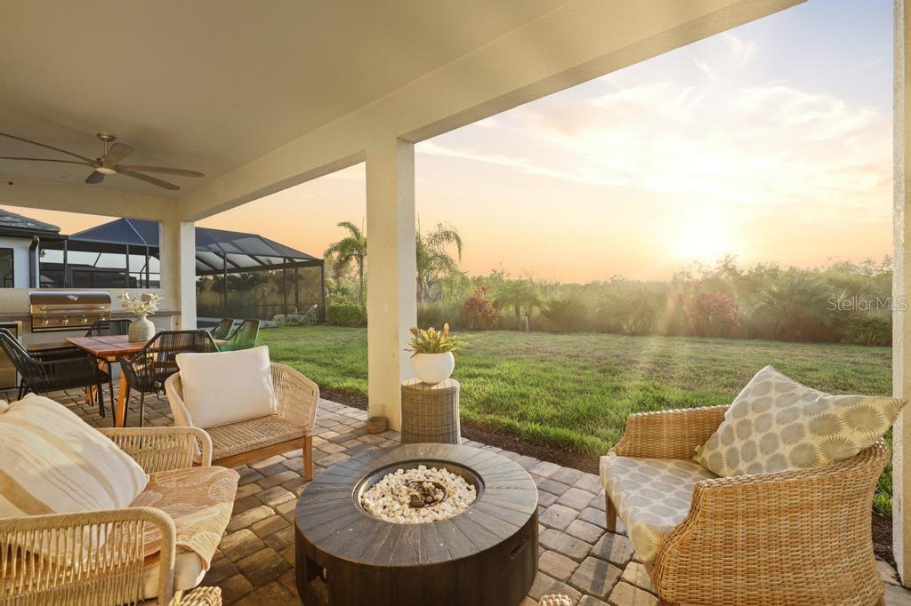 A covered patio features wicker furniture, a fire pit, and an outdoor kitchen overlooking a lawn — 17731 SAVORY MIST CIRCLE, BRADENTON, FL