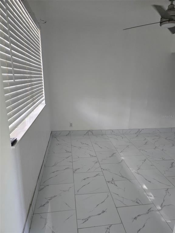 An empty room features white walls, a window with blinds, and white marble-patterned tile flooring — 2630 SW 55TH AVENUE, WEST PARK, FL