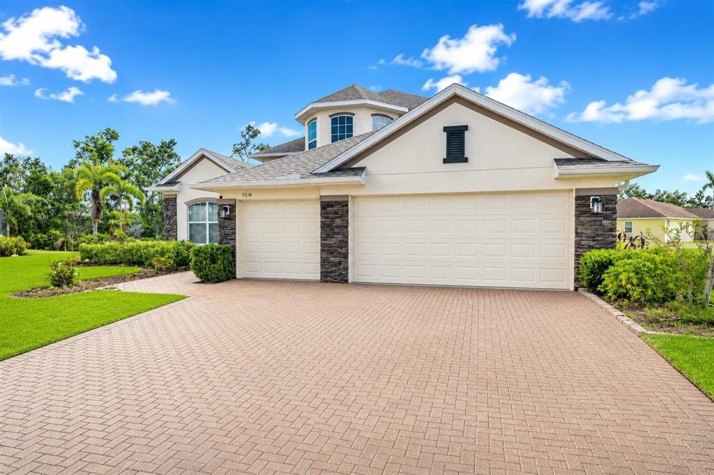 A beige house with a stone-accented facade and a paved driveway under a blue sky — 5518 72ND TERRACE E, ELLENTON, FL