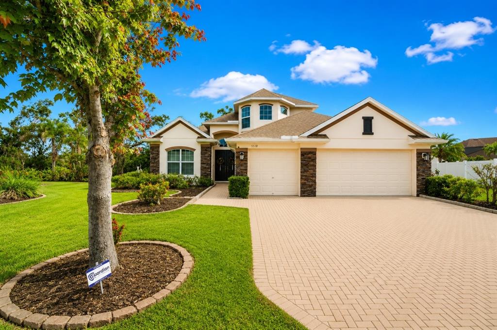 A single-story house with a beige stucco exterior, stone accents, and a paved driveway — 5518 72ND TERRACE E, ELLENTON, FL