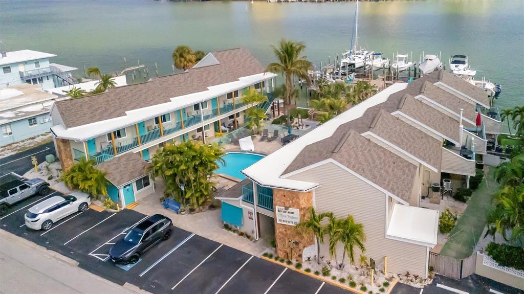 An aerial view shows a multi-story waterfront apartment complex with a pool and boat docks — 673 BAY ESPLANADE UNIT 204, CLEARWATER BEACH, FL