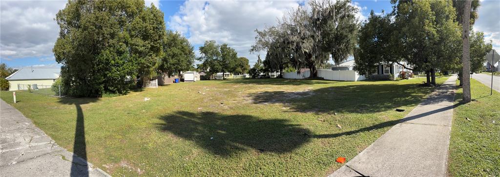 A wide-angle view of a vacant, grassy residential lot bordered by sidewalks and mature trees — 1113 MICHIGAN AVENUE, ST CLOUD, FL