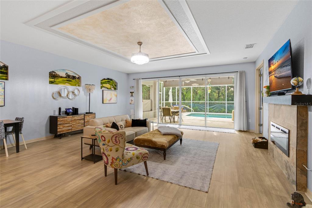 A living room with light wood floors, a fireplace, and sliding doors opening to a pool — 5466 LEGEND HILLS LANE, SPRING HILL, FL