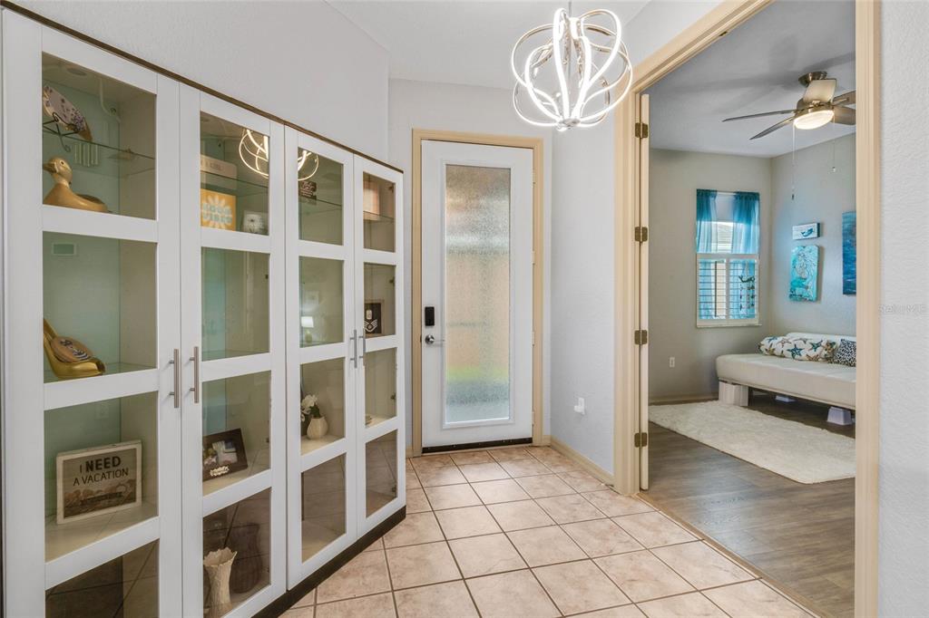 An entryway with tiled floors, a white display cabinet, and a doorway leading to a bedroom — 5466 LEGEND HILLS LANE, SPRING HILL, FL