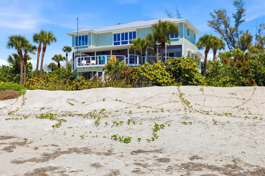 A light green two-story beach house sits behind a sandy dune with palm trees — 400 S GULF BOULEVARD, PLACIDA, FL