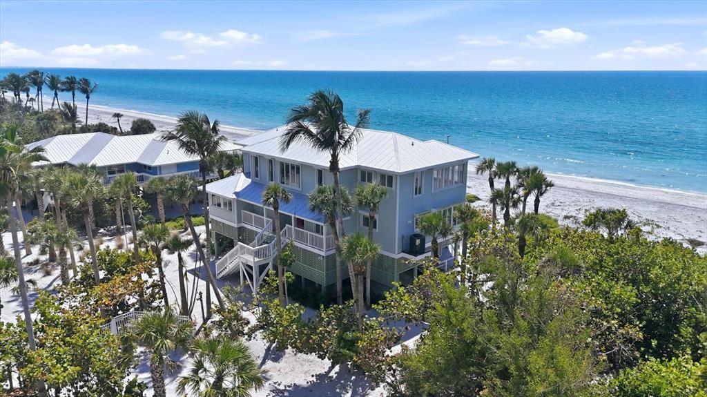 An elevated light blue house sits on a sandy beach surrounded by palm trees — 400 S GULF BOULEVARD, PLACIDA, FL