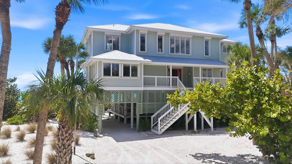 A light green, elevated stilt house with a white porch and stairs on a sandy lot — 400 S GULF BOULEVARD, PLACIDA, FL