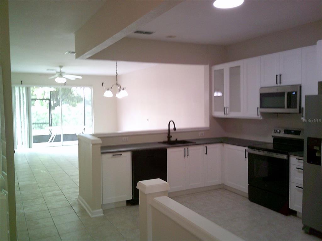 A kitchen with white cabinets and black appliances overlooks a living area with tile floors — 6292 TWAIN STREET UNIT 107, ORLANDO, FL