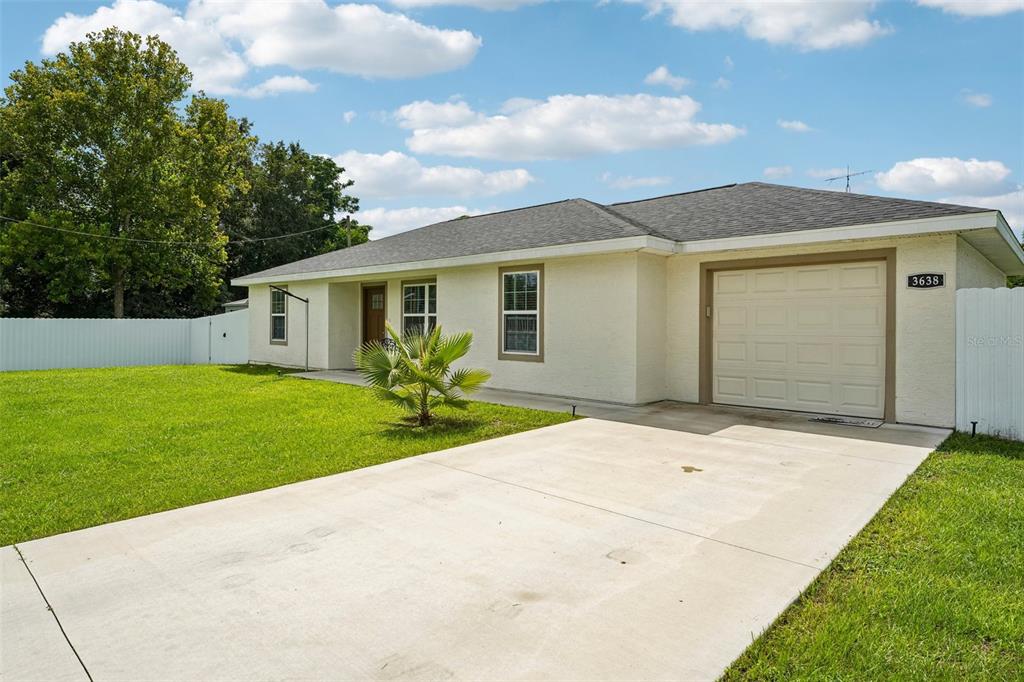 A single-story house with a beige stucco exterior, a concrete driveway, and a white fence — 3638 SE 137TH STREET, SUMMERFIELD, FL