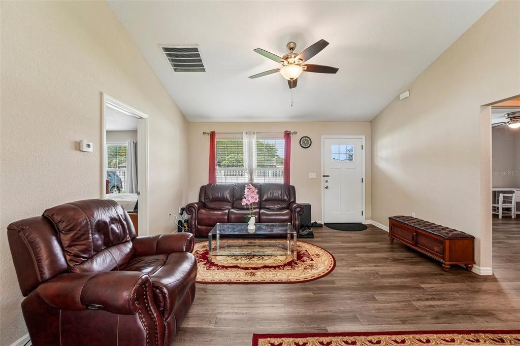 A living room features a vaulted ceiling, wood-look flooring, leather furniture, and a ceiling fan — 3638 SE 137TH STREET, SUMMERFIELD, FL
