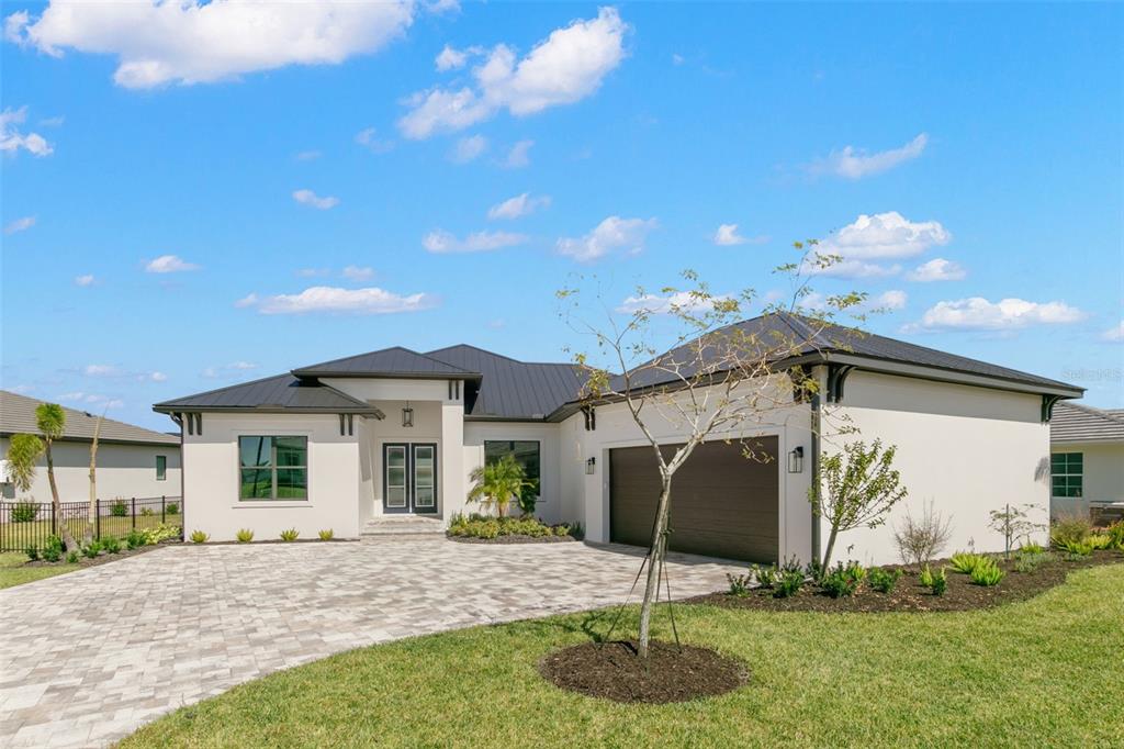 A modern single-story house with a white stucco exterior, dark metal roof, and paved driveway — 1810 4TH STREET E, PALMETTO, FL