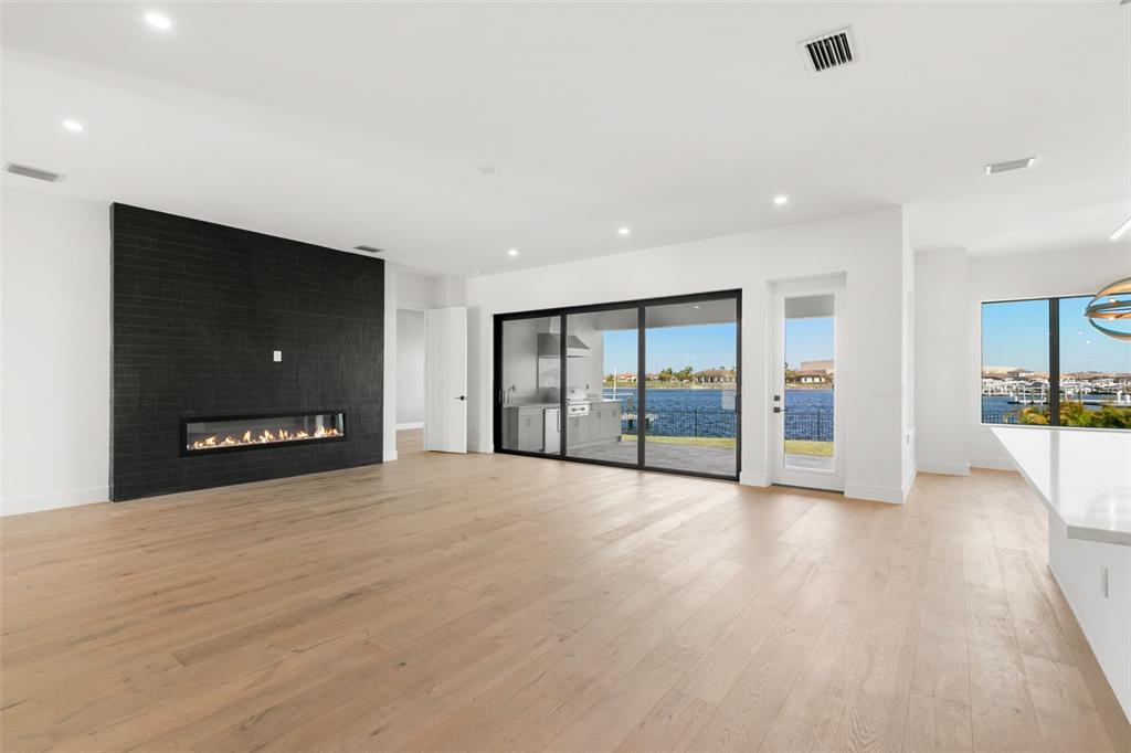 A modern living room features a black tiled fireplace, light wood floors, and sliding glass doors — 1810 4TH STREET E, PALMETTO, FL