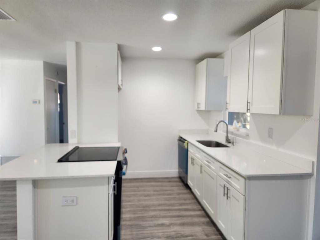 A kitchen features white cabinets, white countertops, a stainless steel sink, and a cooktop island — 800 DIANE CIRCLE, CASSELBERRY, FL