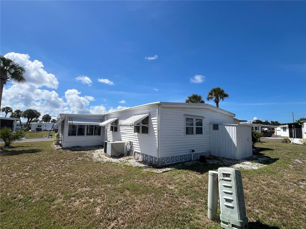 A white mobile home with metal awnings sits on a grassy lot under a blue sky — 633 COMO DRIVE, VENICE, FL