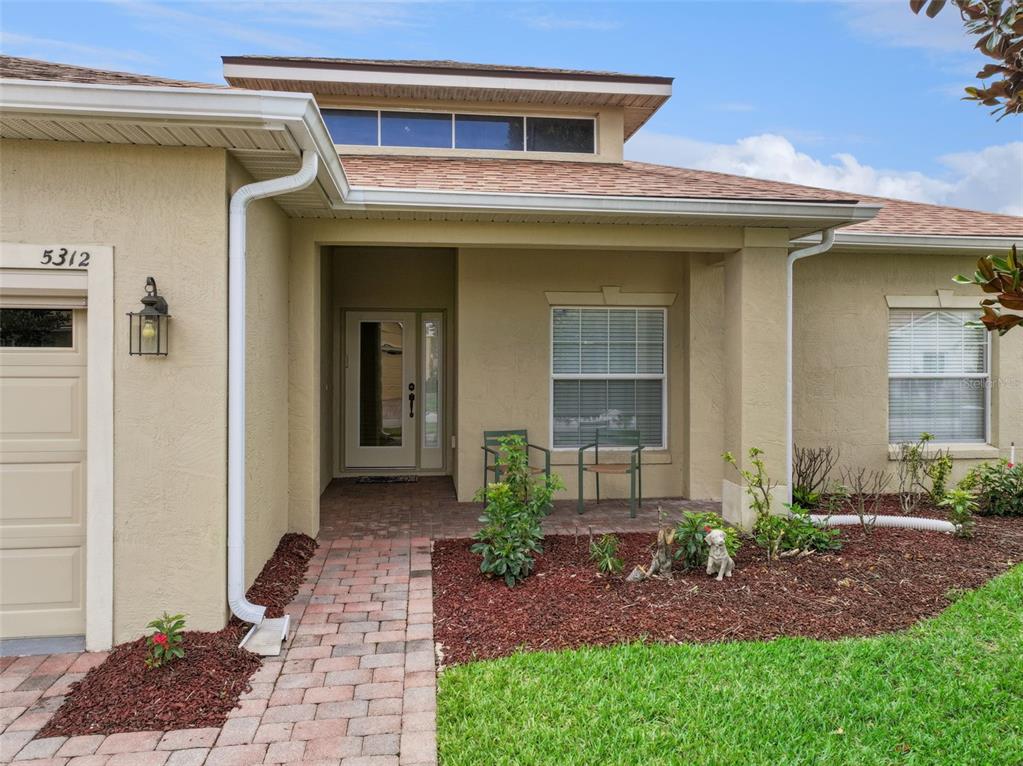 The exterior of a tan house features a brick walkway, a covered entryway, and two windows — 5312 NICKLAUS DRIVE, WINTER HAVEN, FL