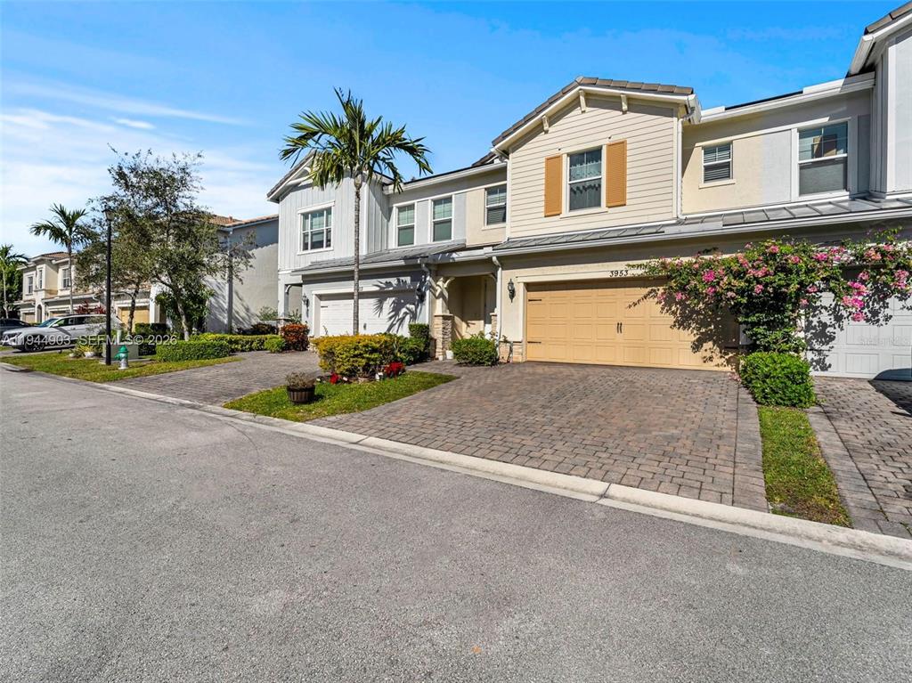 A two-story townhouse features a tan garage, paved driveway, and a small front garden — 3953 BLACK OLIVE LANE, HOLLYWOOD, FL