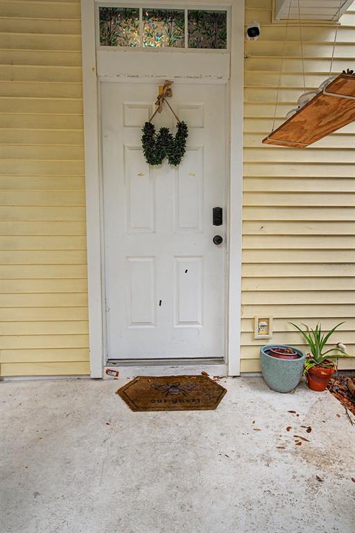 A white front door with a wreath, a welcome mat, and potted plants on a porch — 2214 GOLDEN OAK LANE, VALRICO, FL