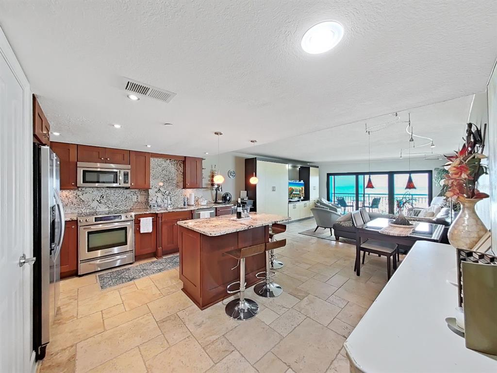 A living room features a large television, leather sofa, armchairs, and floor-to-ceiling windows overlooking the ocean — 19440 GULF BOULEVARD UNIT 104, INDIAN SHORES, FL