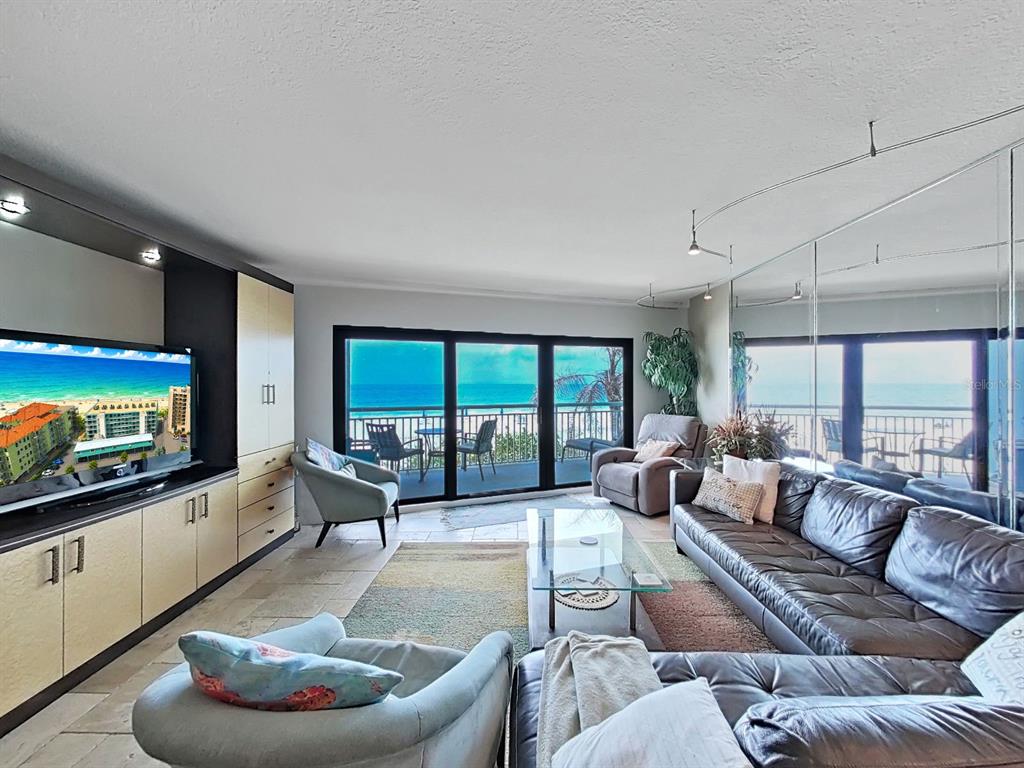 A living room features tile floors, a large sectional sofa, and floor-to-ceiling windows overlooking the ocean — 19440 GULF BOULEVARD UNIT 104, INDIAN SHORES, FL